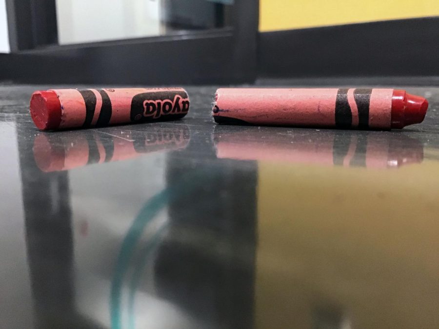 A broken red crayon lies on a classroom floor.